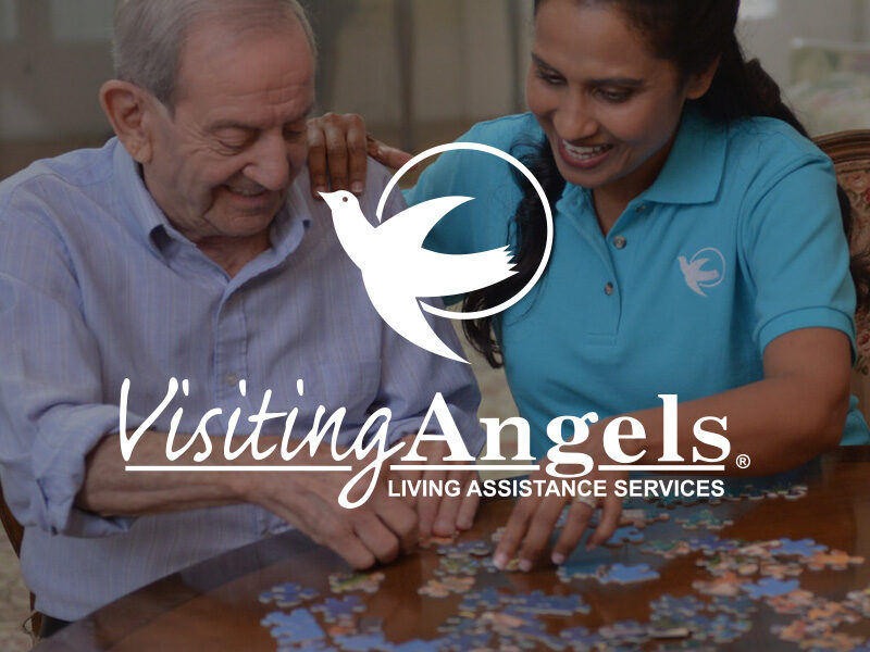 Elderly man making a puzzle with the assistance of a Visiting Angels caretaker.