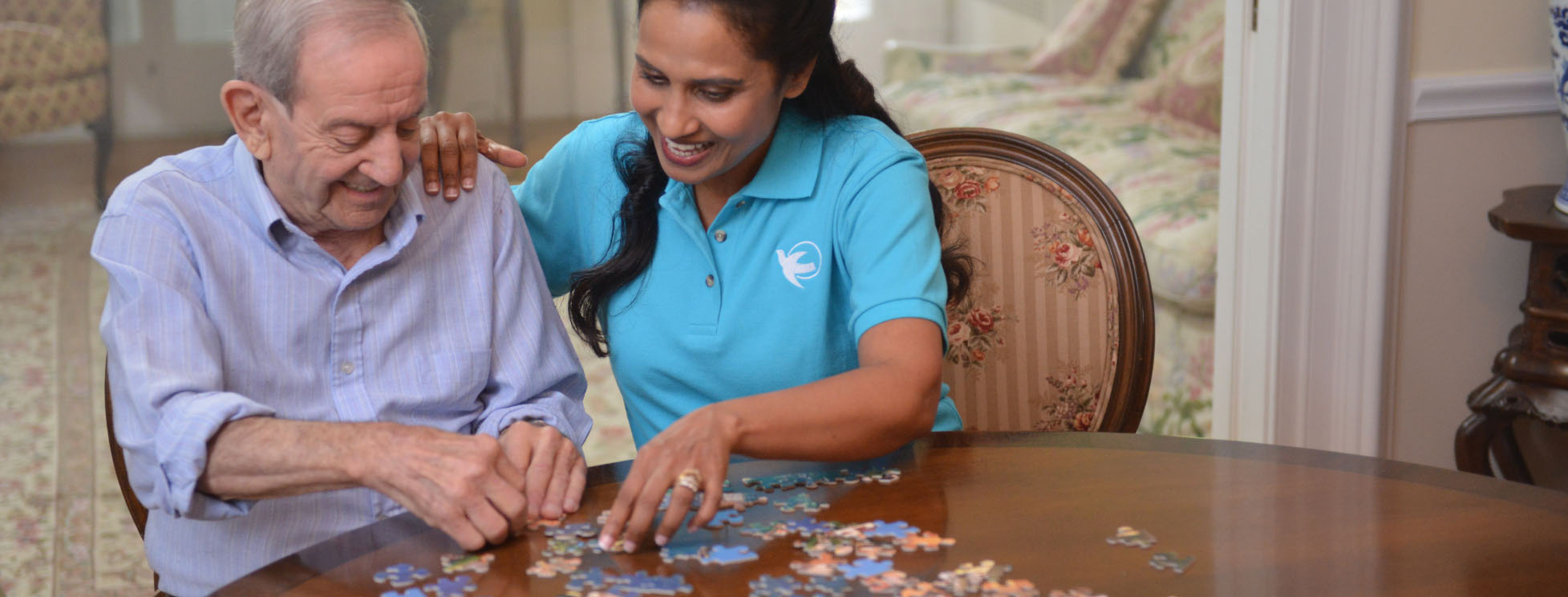 Visiting Angels caretaker helping elderly man put together a puzzle.