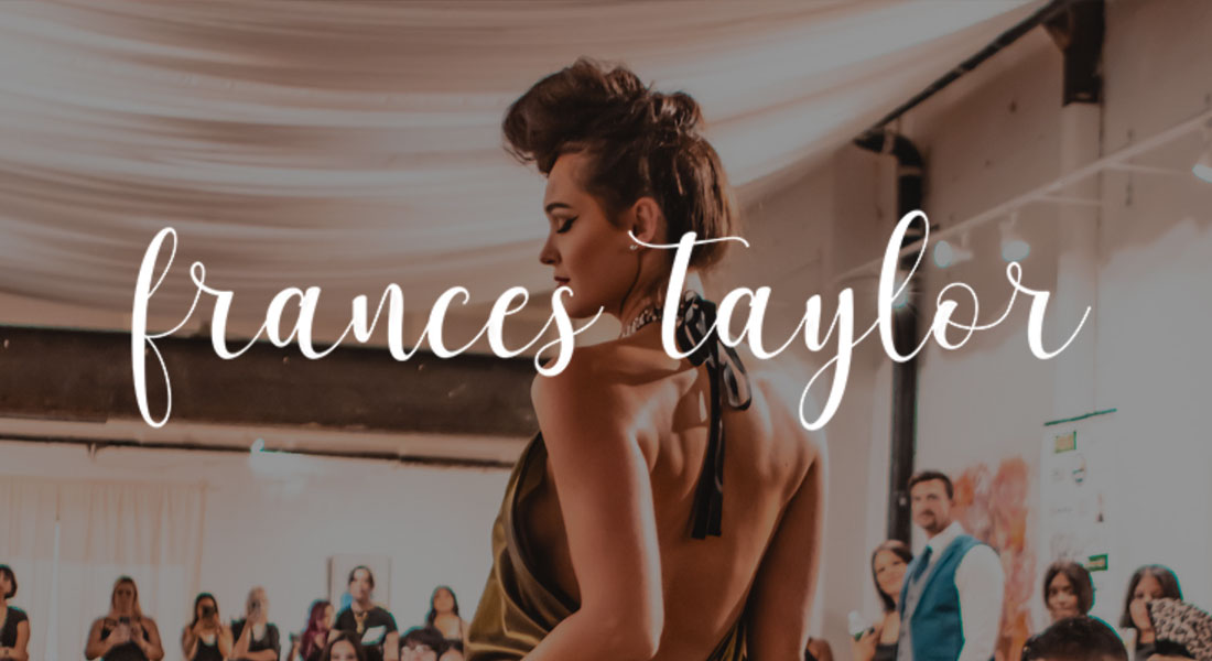Woman in an elegant backless halter dress walking a runway at an indoor fashion show, with spectators and draped fabric ceiling in the background.